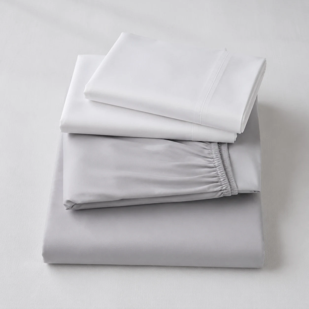 Folded cotton bed sheets and pillowcases arranged in neutral tones