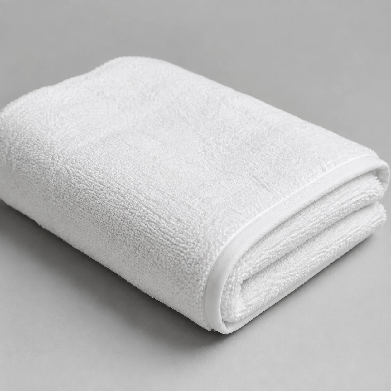 Folded white Egyptian cotton bath sheet with deep looped pile on a pale grey surface