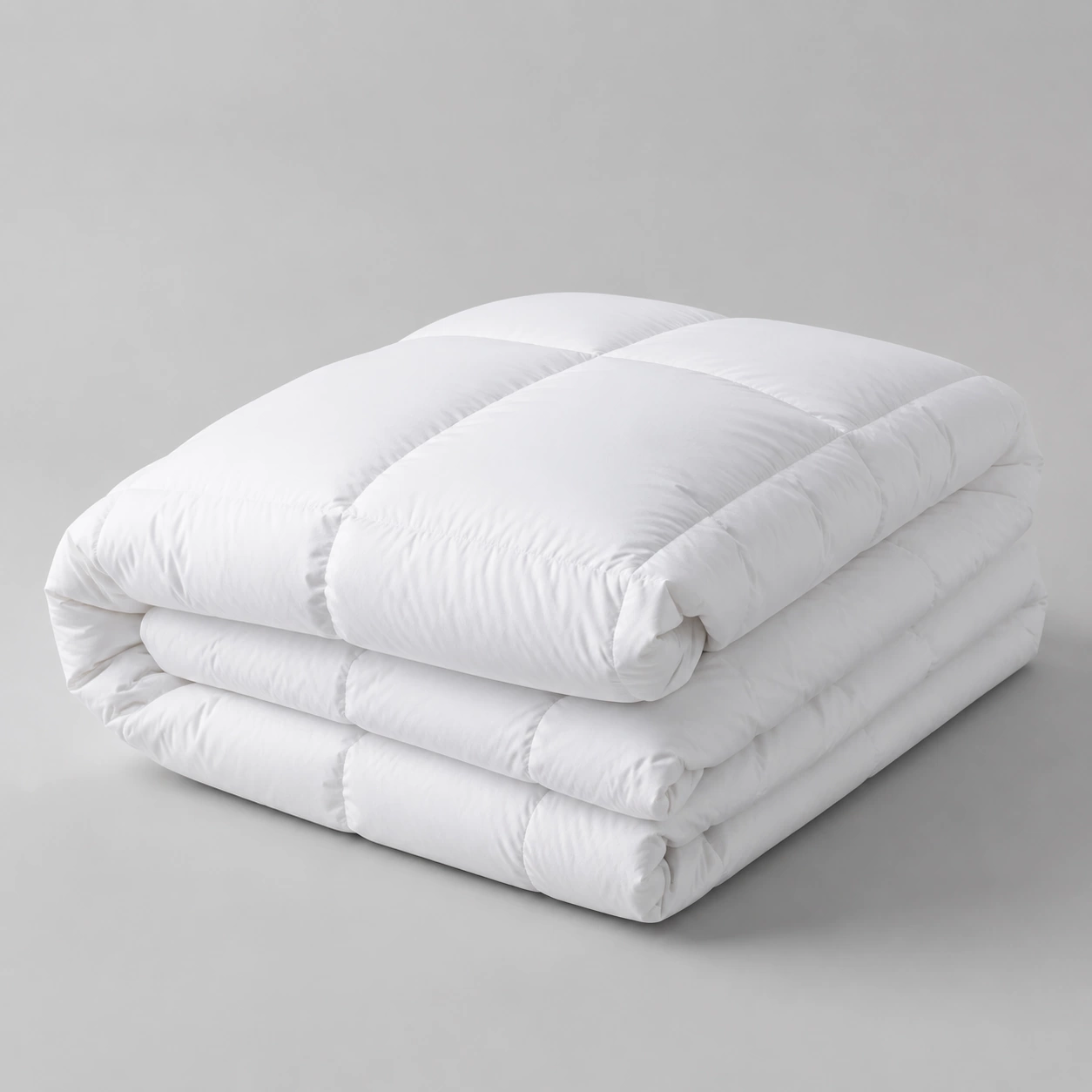 Folded white hollowfibre duvet showing quilted stitch channels on a pale grey surface
