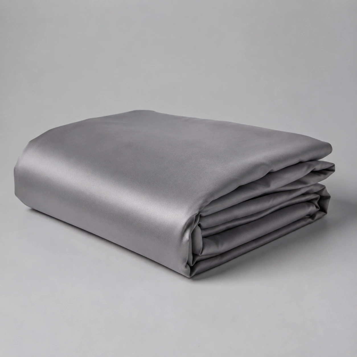 Folded soft grey sateen duvet cover on a pale grey surface