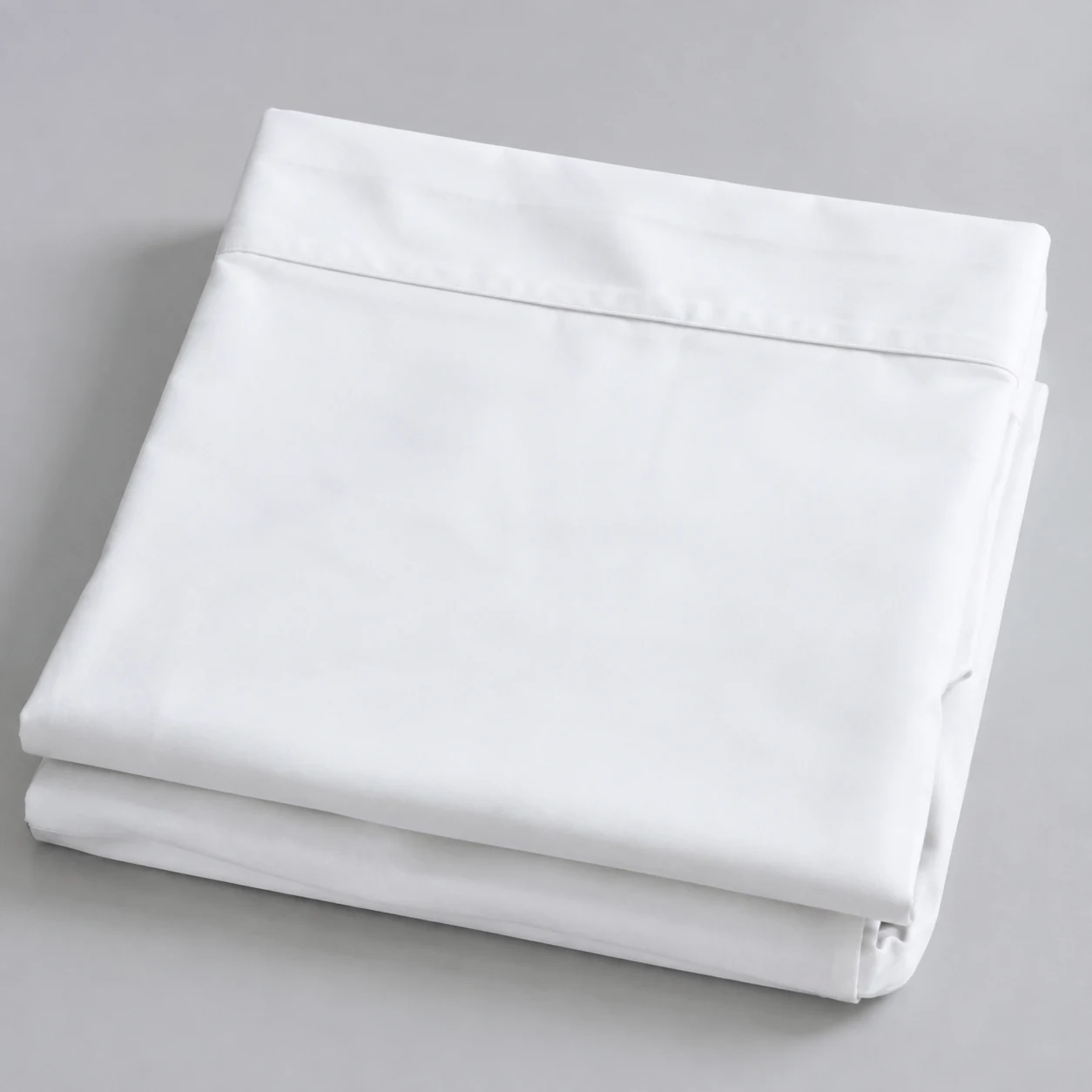 Folded white percale cotton flat sheet with a wide top hem on a pale grey surface