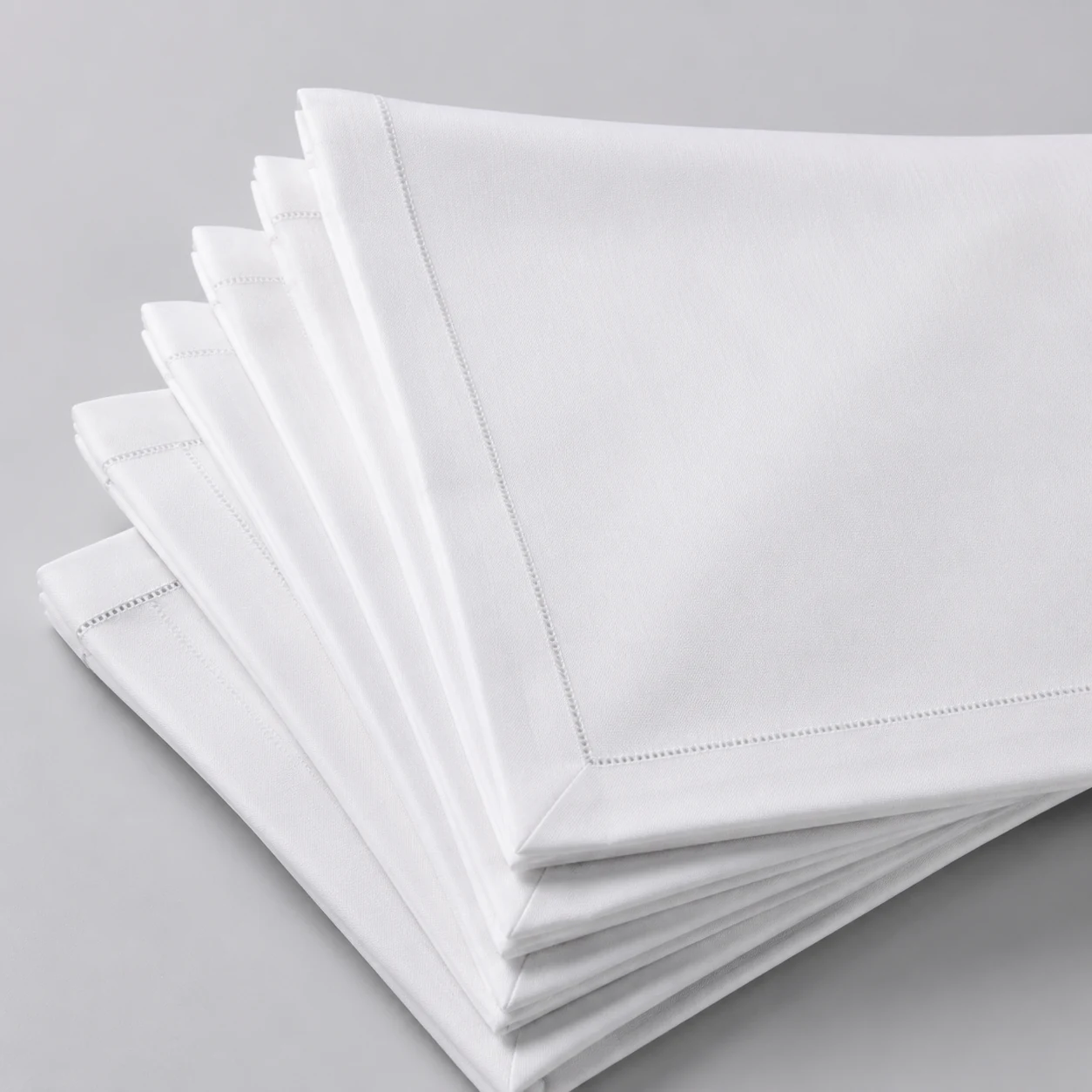 Fanned stack of folded white hemmed cotton napkins on a pale grey surface