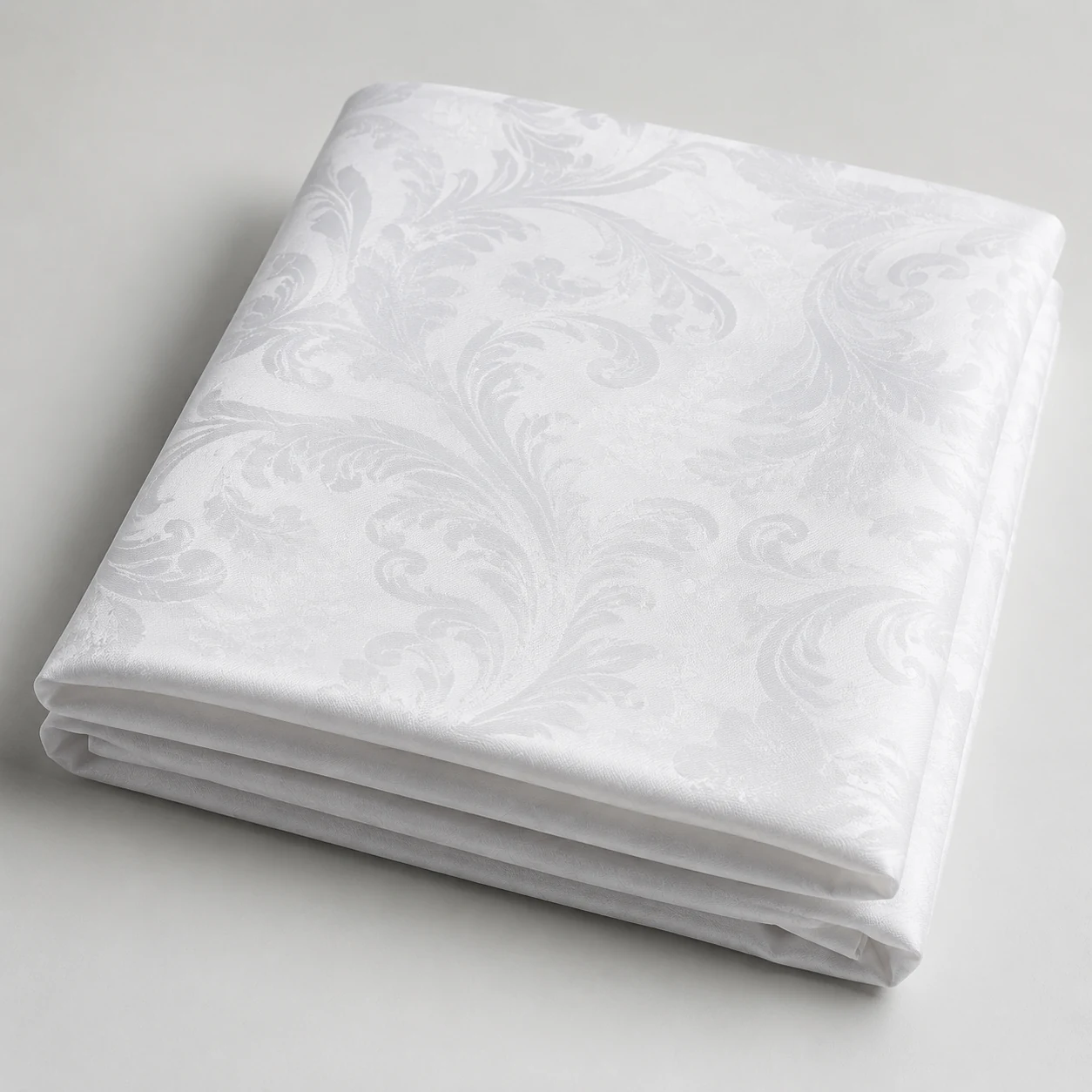 Folded white cotton damask tablecloth on a pale grey surface